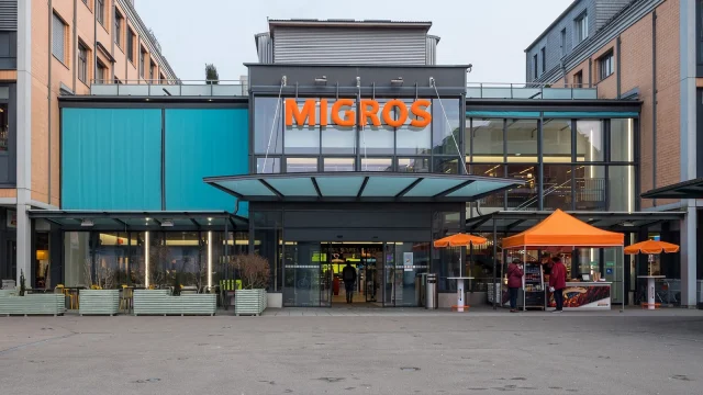 Intérieur d'un supermarché Migros avec caisses et personnel.